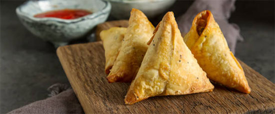 Les samoussas sont des beignets triangulaires à base de pâte phyllo, originaires d'Asie centrale et du Moyen-Orient. Ils sont devenus un mets populaire dans le sous-continent indien depuis qu'ils y ont été introduits par les Arabes au Moyen Âge.
